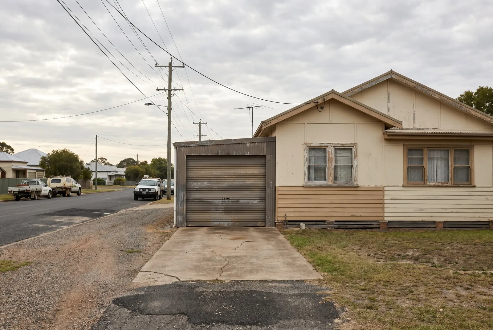 An older fibro cottage on a quiet street with a weathered roller door on its garage